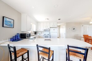 Une cuisine moderne avec des meubles blancs, un îlot central et un coin repas doté de chaises en bois.