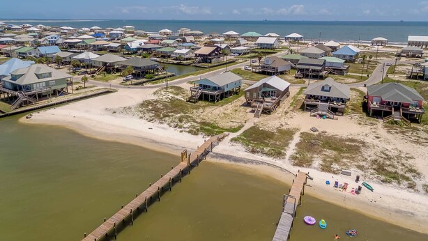 An aerial view of a coastal residential area with houses, a beach, and a pier. - Welcoming home with WiFi, gulf views & spacious deck - steps to the beach (Dauphin Island)