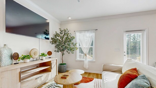 A modern living room with a flat-screen TV, a wooden console table with decorative items, a round coffee table, a sofa with colorful cushions, and a large potted plant. - Dog friendly home near the Wharf with internet and free parking (Orange Beach)