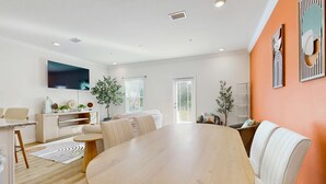 A modern living room with a wooden dining table, white sofas, a flat-screen TV, and a large window. - Dog friendly home near the Wharf with internet and free parking (Orange Beach)