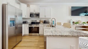 A modern kitchen with white cabinets, stainless steel appliances, a granite countertop, and a flat-screen TV mounted above the sink. - Dog friendly home near the Wharf with internet and free parking (Orange Beach)