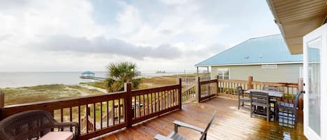 A wooden deck with outdoor furniture, a view of the beach, and a building with a blue roof.