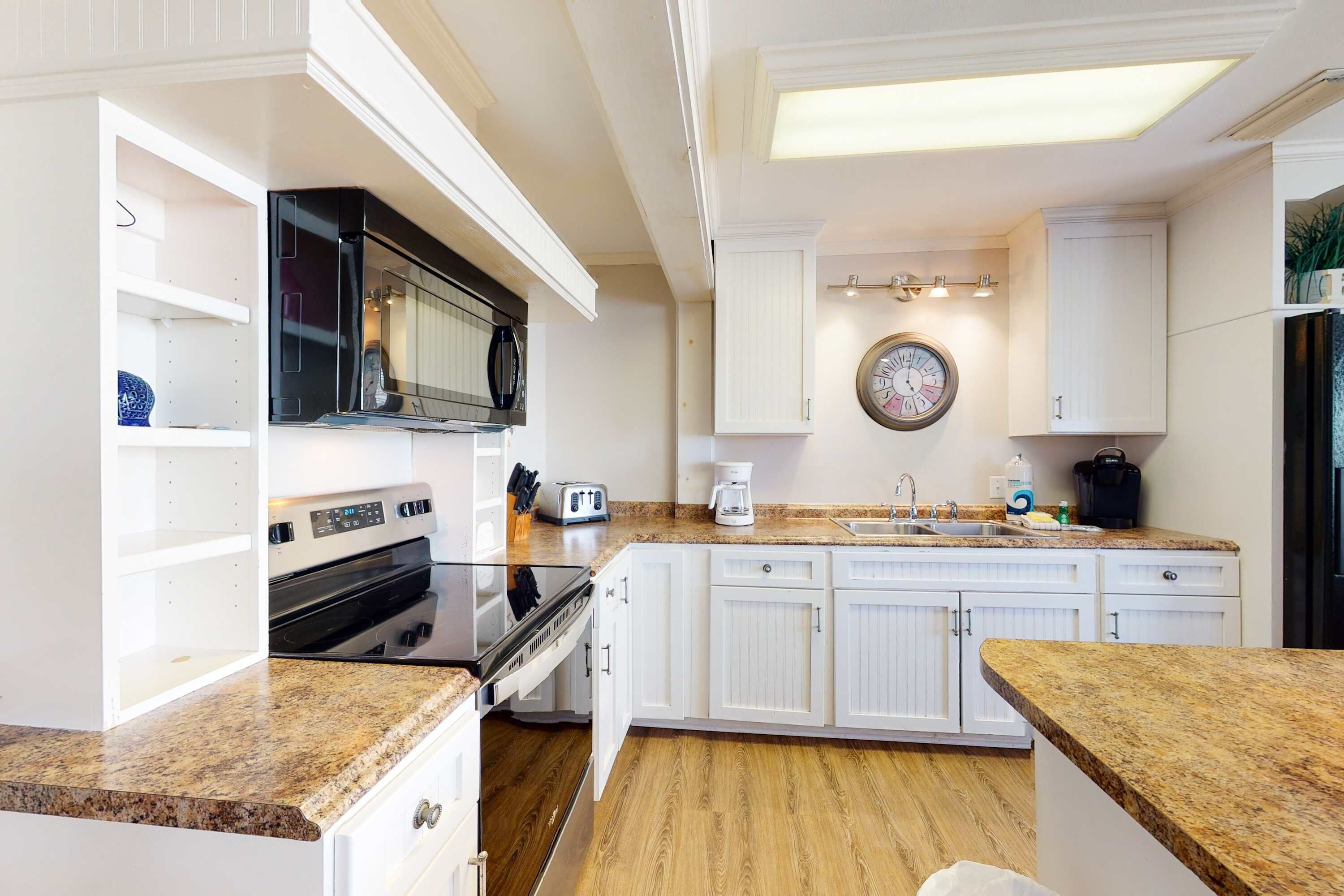 A kitchen with white cabinetry, a microwave, a toaster, a coffee maker, and a sink.