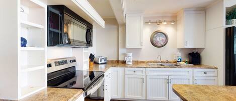 A kitchen with white cabinetry, a microwave, a toaster, a coffee maker, and a sink.