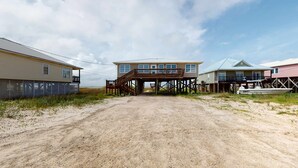 Propiedad frente a la playa con camino de tierra que lleva a una terraza de madera, un bote y dos casas con estructuras elevadas.