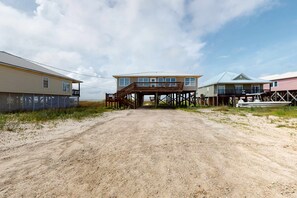 A beachfront property with a dirt road leading to a wooden deck, a boat, and two houses with elevated structures. - Dog-friendly home with sound-side deck, full kitchen, & fantastic views (Dauphin Island)
