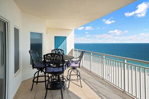A balcony with a table and chairs, a view of the ocean, and a blue door. - Upscale beachfront retreat w/private balcony, resort pool, sauna, & beach access (Orange Beach)