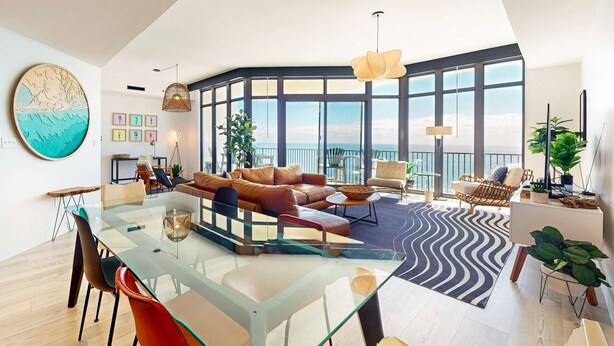 Un amplio salón con mesa de vidrio, sofás de cuero y grandes ventanales con vistas al cielo.