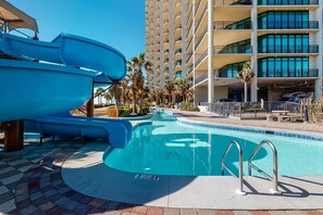 A swimming pool with a water slide, palm trees, and a multi-story building with balconies. - Gulf front condo with direct beach access, resort amenities, private W&D, WiFi (Orange Beach)