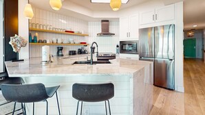 Una cocina moderna con armarios blancos, una isla central con taburetes de bar, electrodomésticos de acero inoxidable e iluminación colgante.