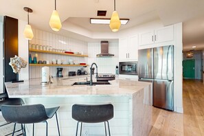 A modern kitchen with white cabinetry, a central island with bar stools, stainless steel appliances, and pendant lighting. - Gulf front condo with direct beach access, resort amenities, private W&D, WiFi (Orange Beach)