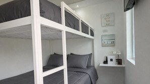 A bunk bed room with grey bedding, a small shelf with a white appliance, and motivational wall art. - Tierra Serena - Private Nature Retreat (Rincón)
