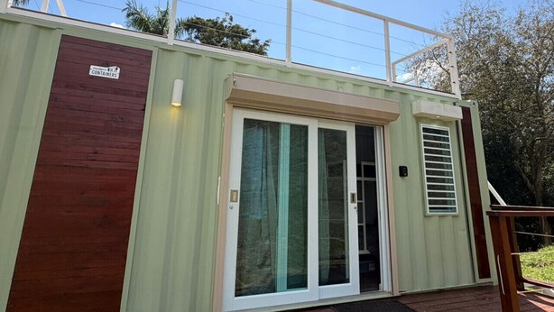 A modern container home with a sliding glass door, a wooden deck, and a metal railing. - Tierra Serena - Private Nature Retreat (Rincón)