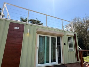 A modern container home with a sliding glass door, a wooden deck, and a metal railing. - Tierra Serena - Private Nature Retreat (Rincón)