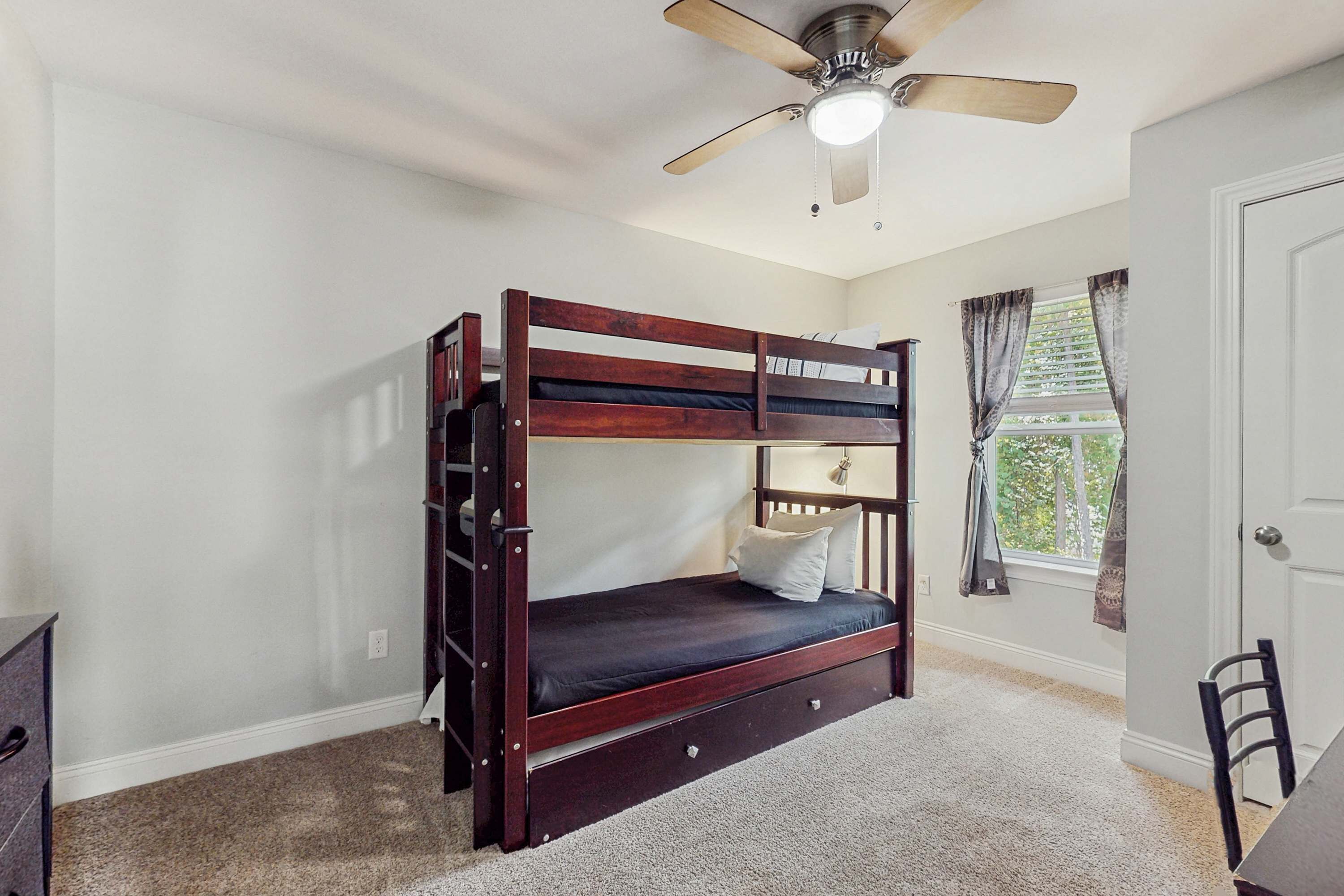 A bunk bed with a ceiling fan, a window with curtains, and a door.