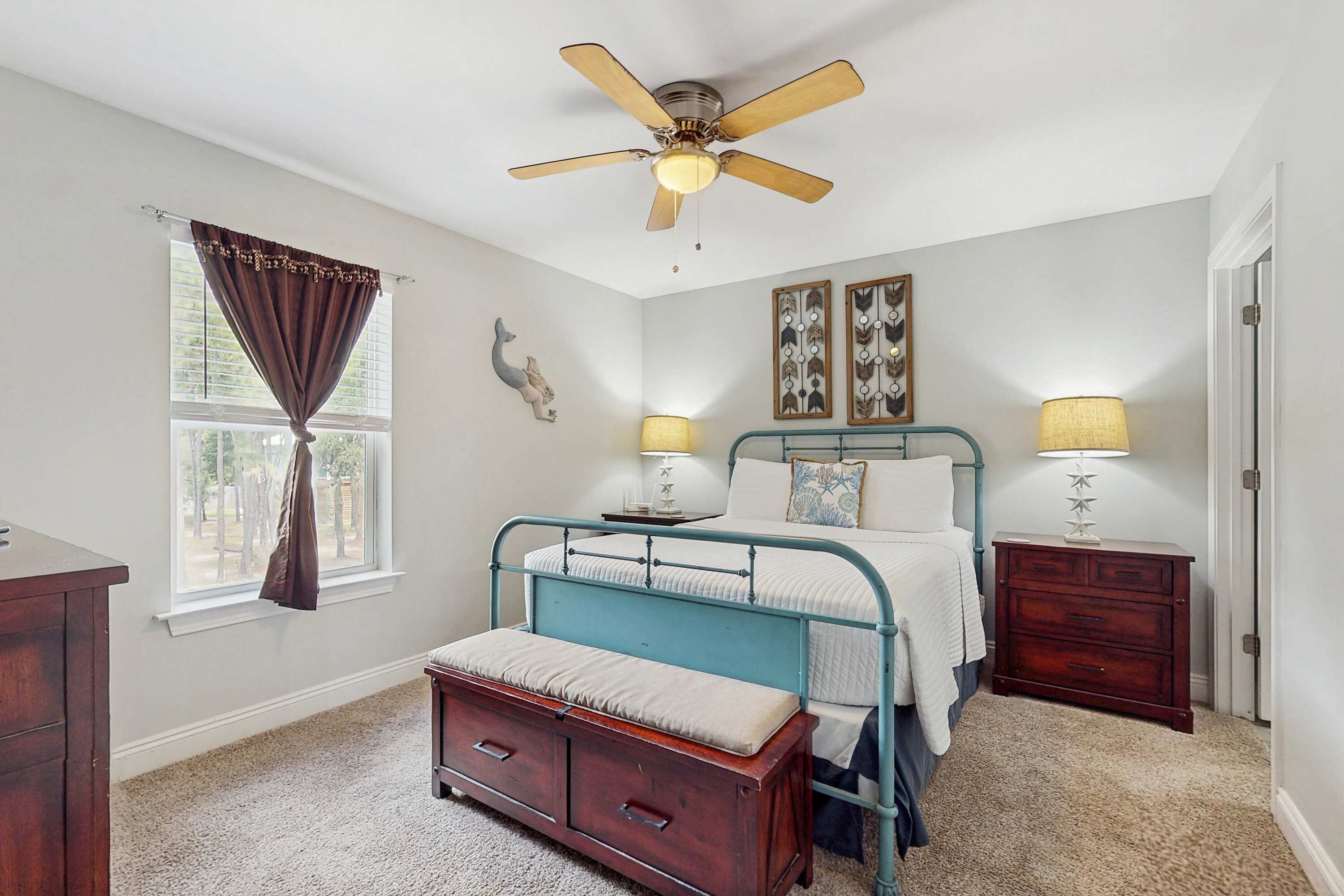 Un dormitorio con cama, lámparas de noche, ventilador de techo, ventana con cortinas y cómoda.