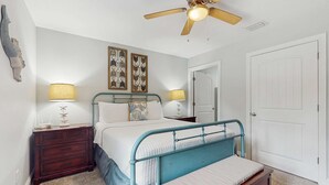 Une chambre à coucher avec un lit, des tables de chevet, un ventilateur de plafond et une porte.