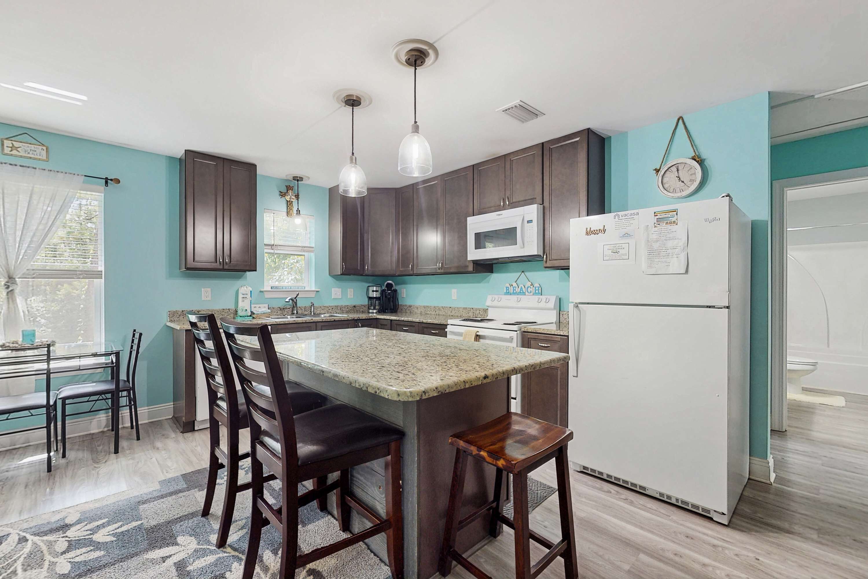 A kitchen with dark wooden cabinets, a white refrigerator, a microwave, and a large island with bar stools.