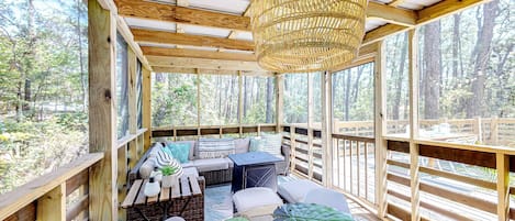 Una terraza de madera con zona de estar, incluyendo sofás y mesas, y un colgador de luces.