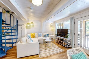 Un salon spacieux avec un canapé blanc, un escalier bleu et un téléviseur.