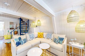 Un salon moderne avec un canapé d’angle, des tables basses rondes et un escalier doté de rampes bleues.