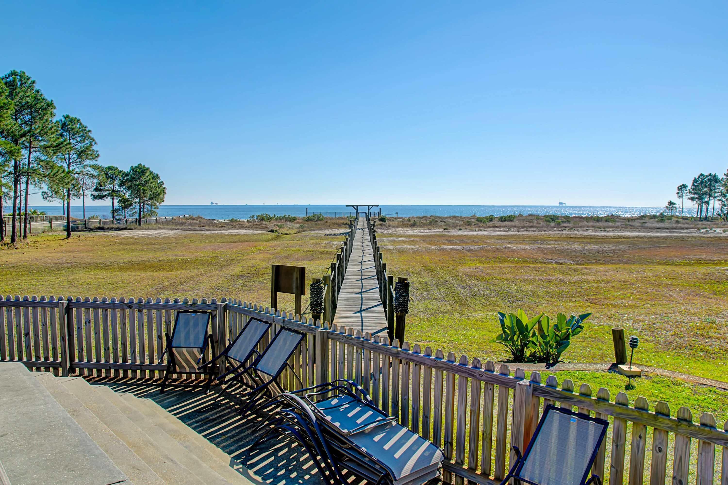 A wooden deck with lounge chairs and a pathway leading to a beach.