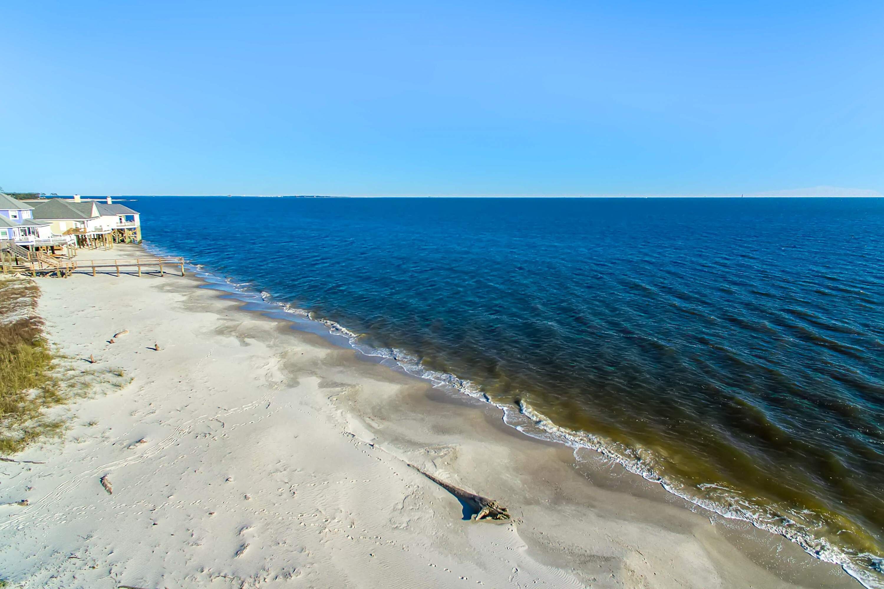 Una playa con un paseo de madera que conduce a una hilera de casas.