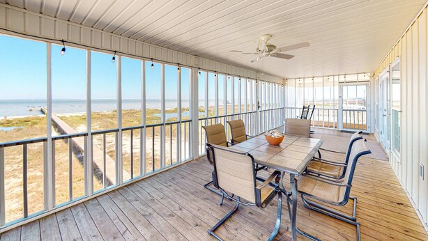 A covered outdoor area with a table and chairs, large windows, and a ceiling fan. - Bayfront retreat with lovely views, a screened porch & beach access (Dauphin Island)