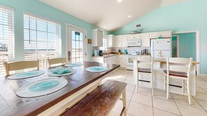 A modern kitchen with white cabinets, a wooden dining table with placemats, and a view through the window. - Bayfront retreat with lovely views, a screened porch & beach access (Dauphin Island)