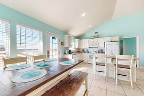 A modern kitchen with white cabinets, a wooden dining table with placemats, and a view through the window. - Bayfront retreat with lovely views, a screened porch & beach access (Dauphin Island)
