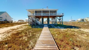 A beach house with a wooden deck leading to a covered porch. - Bayfront retreat with lovely views, a screened porch & beach access (Dauphin Island)