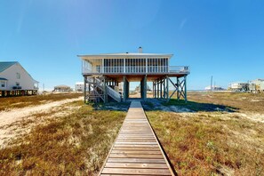 A beach house with a wooden deck leading to a covered porch. - Bayfront retreat with lovely views, a screened porch & beach access (Dauphin Island)