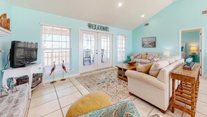 A living room with a sofa, television, decorative birds, and a welcome sign. - Bayfront retreat with lovely views, a screened porch & beach access (Dauphin Island)