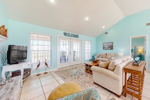 A living room with a sofa, television, decorative birds, and a welcome sign. - Bayfront retreat with lovely views, a screened porch & beach access (Dauphin Island)