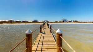 A wooden pier leading to a beach with buildings in the background. - Bayfront retreat with lovely views, a screened porch & beach access (Dauphin Island)
