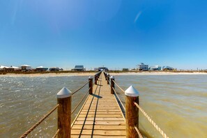 A wooden pier leading to a beach with buildings in the background. - Bayfront retreat with lovely views, a screened porch & beach access (Dauphin Island)