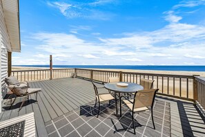 Eine Terrasse mit Tisch und Stühlen, Blick auf den Strand und ein Holzzaun.