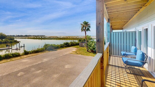 Una terraza de madera con sillas azules, vista a un lago y un cobertizo pequeño.