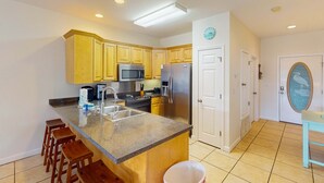 Una cocina con armarios de madera, electrodomésticos de acero inoxidable, encimera de granito y una zona con taburetes de bar.