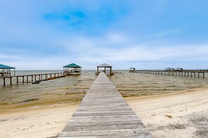 Eine Holzsteg, der zu einem Strand mit zwei Lauben und einem klaren Himmel führt.