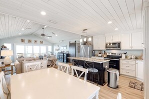 A spacious kitchen with white cabinetry, a large island with bar stools, a microwave, and a stainless steel refrigerator. - Waterfront beach house on the sound with breathtaking sunset views & gulf access (Dauphin Island)