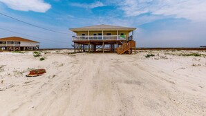 Ein Strandhaus mit Balkon, Holzterrasse und einem Sandstrand im Hintergrund.