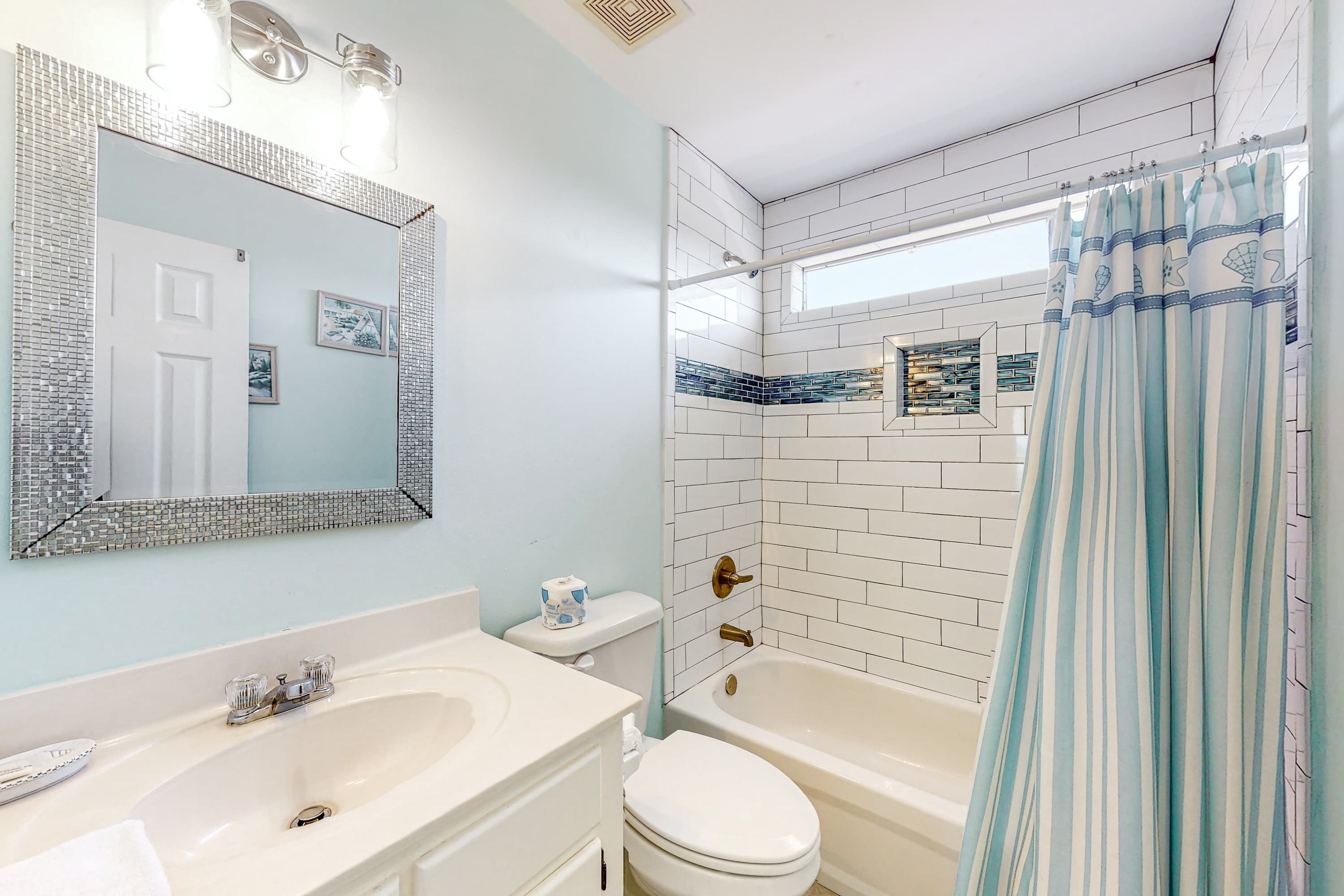 Un baño con lavamanos, inodoro y bañera blancos, un espejo grande y una cortina de ducha con diseño a rayas.