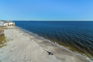 A beach with a wooden pier leading to a row of houses. - Dog-friendly beach house with fantastic location, access to water (Dauphin Island)