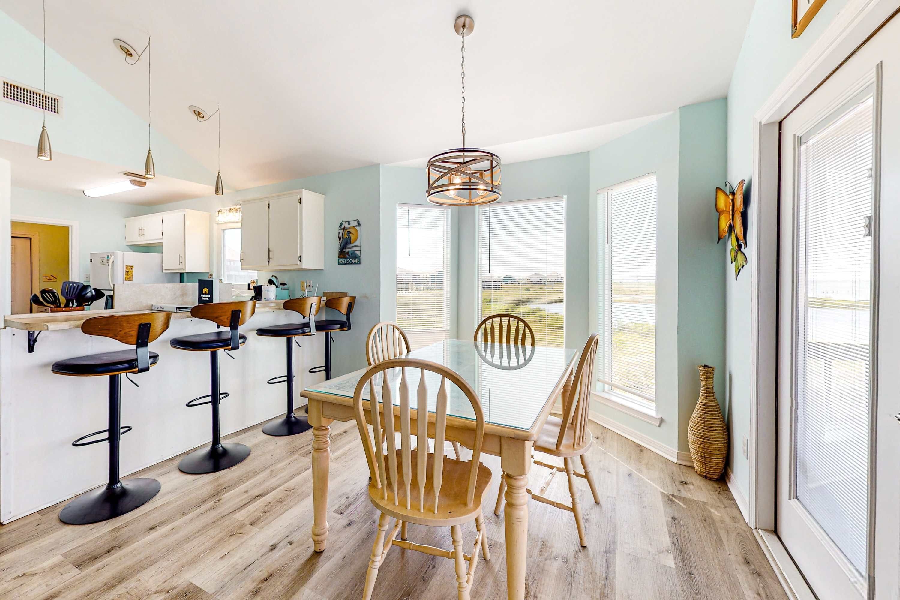 Une cuisine moderne avec une table à manger en verre, des chaises en bois et des luminaires suspendus.