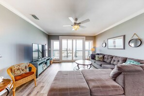 Ein Wohnzimmer mit Sofa, Fernseher, Deckenventilator und Balkonblick.