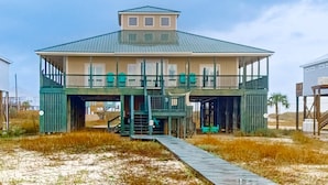 A beachfront house with a covered deck, a staircase leading to an upper level, and a pathway to the entrance. - Bayfront home with wraparound deck & great water views - dog-friendly (Dauphin Island)