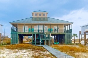 Ein Strandhaus mit überdachter Terrasse, einer Treppe zu einem oberen Stockwerk und einem Weg zum Eingang.