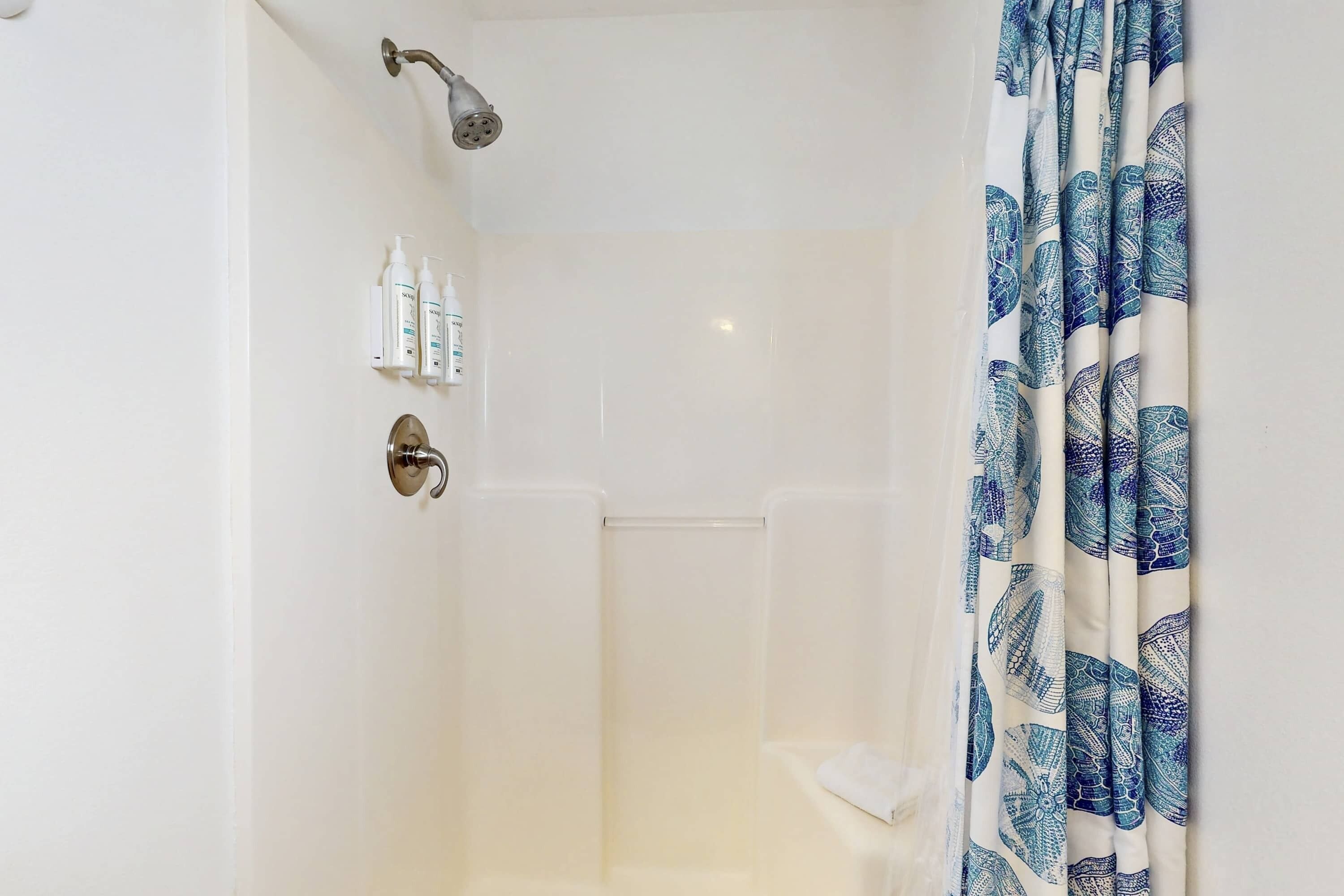 A shower with a handheld showerhead, a glass door, and a blue patterned shower curtain.