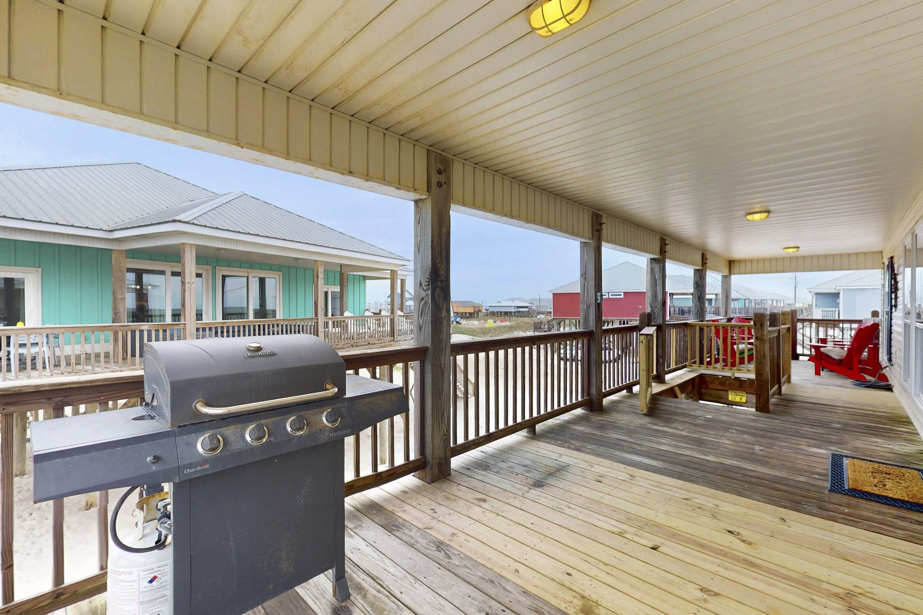 A covered outdoor area with a grill, wooden deck, and a view of buildings in the background.